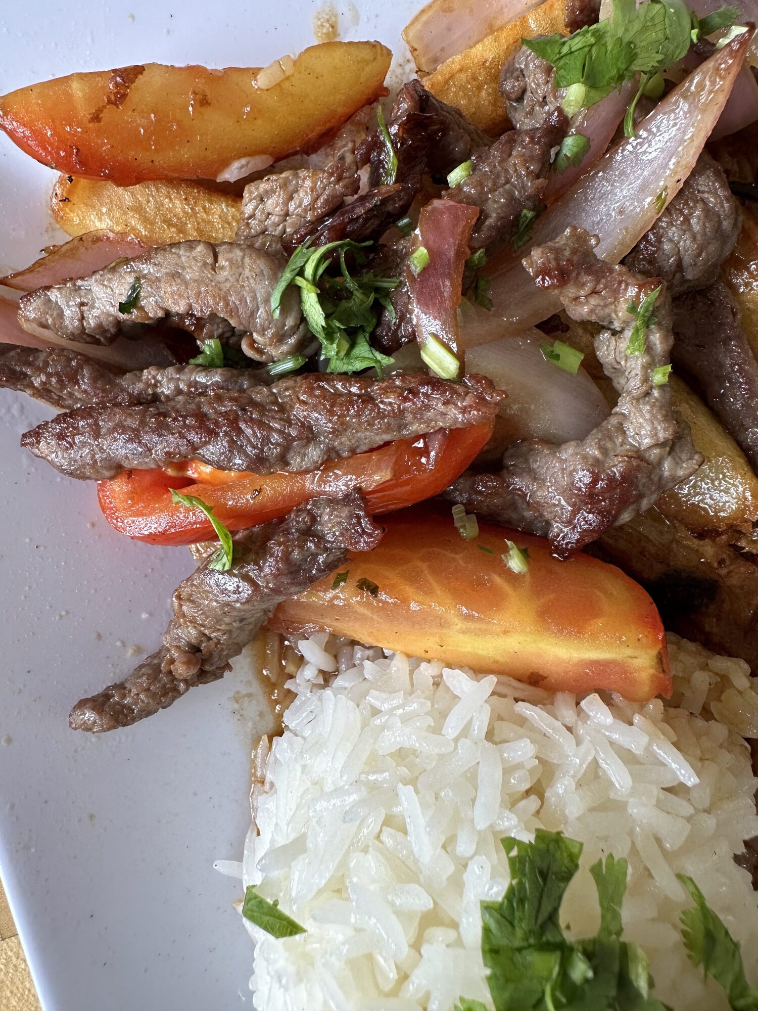 Peruvian lomo saltado — strips of steak stir-fried with red onion and tomato, served with fried potatoes and white rice.