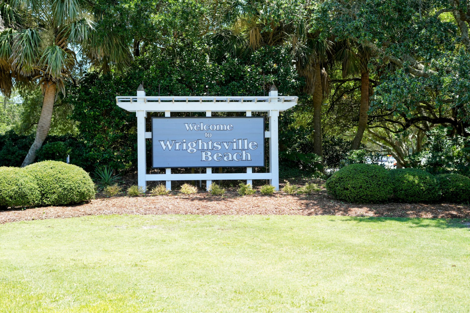 Welcome to Wrightsville Beach sign amid palms and live oaks in Wrightsville Beach, NC.