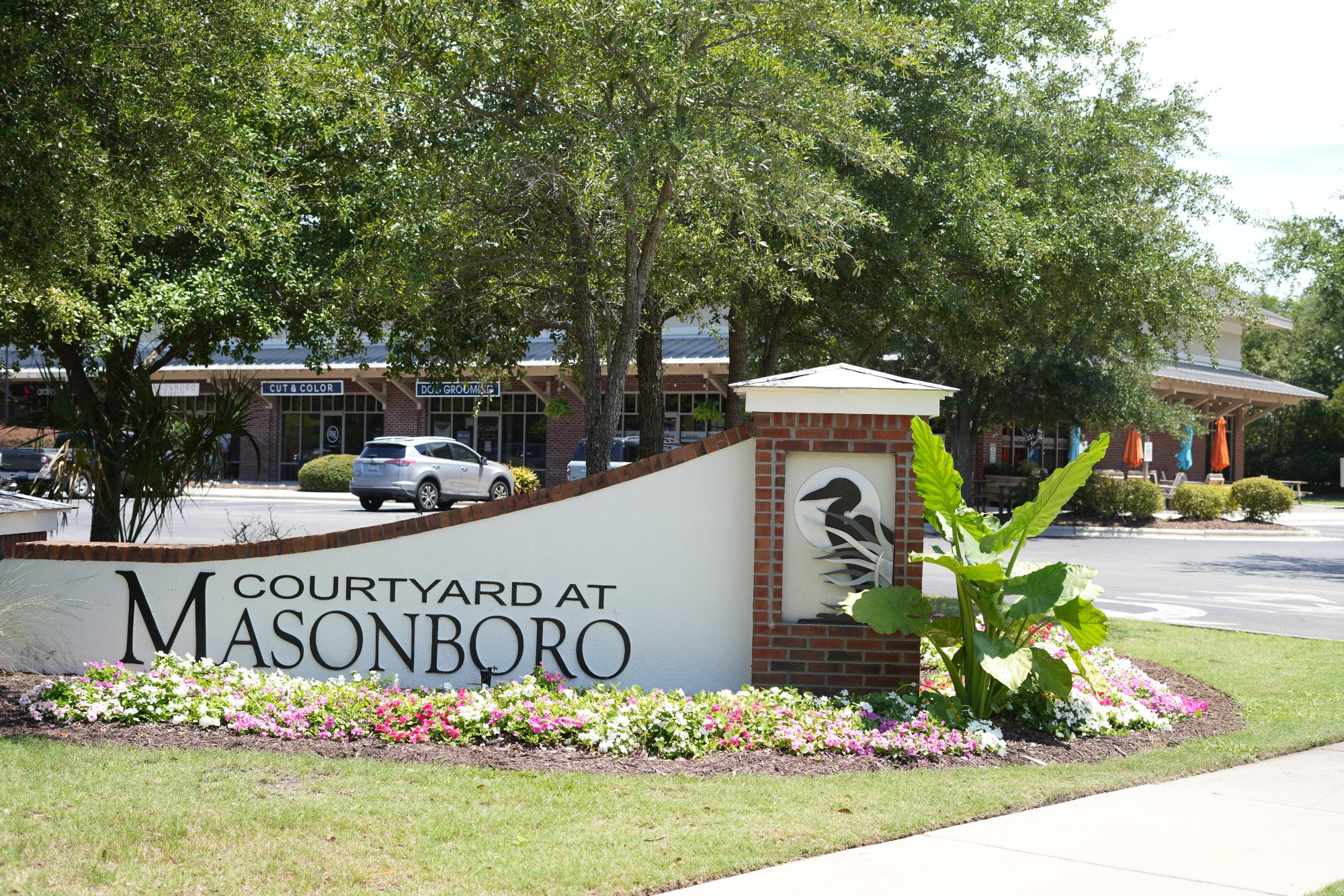"Courtyard at Masonboro" brick-and-stucco monument sign with flowers at a Wilmington, NC shopping center.