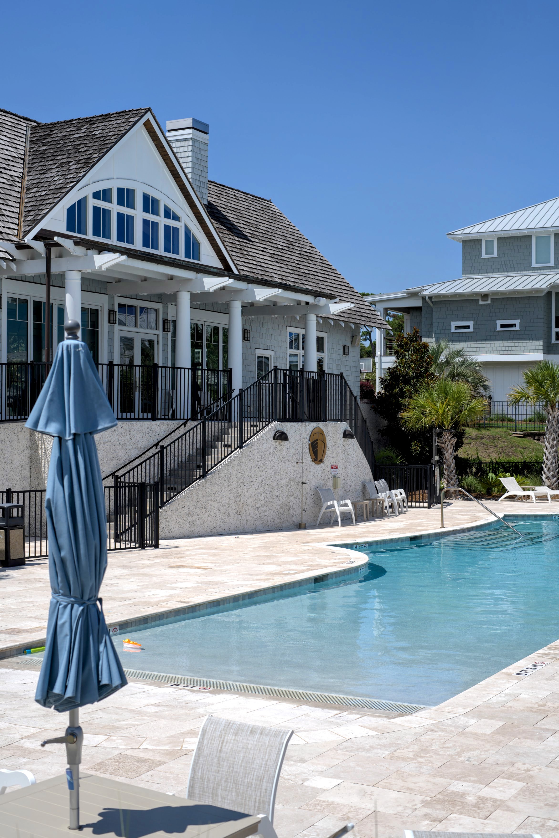 Resort-style community pool with a lounge umbrella and shingled clubhouse in the Masonboro / Greenville Loop area of Wilmington, NC.