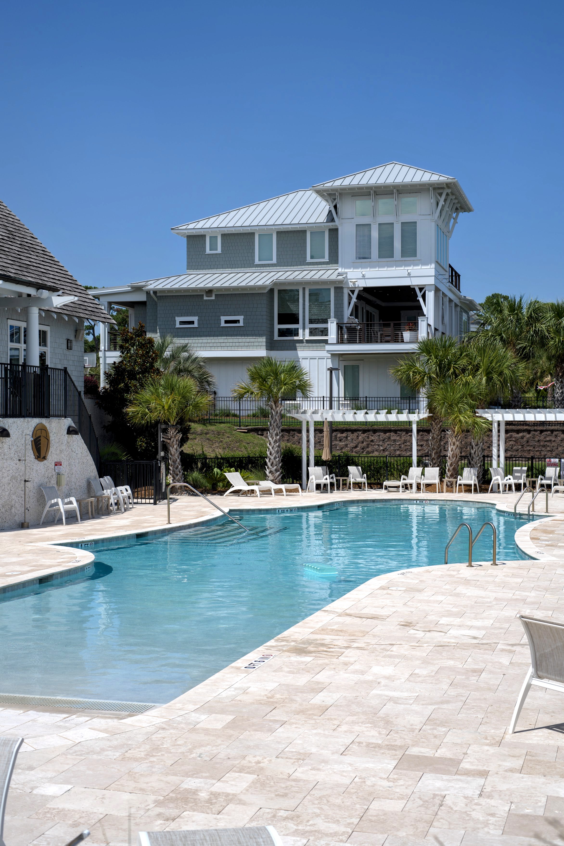 Community swimming pool beside a modern gray coastal home on a sunny day in the Masonboro / Greenville Loop area of Wilmington, NC.