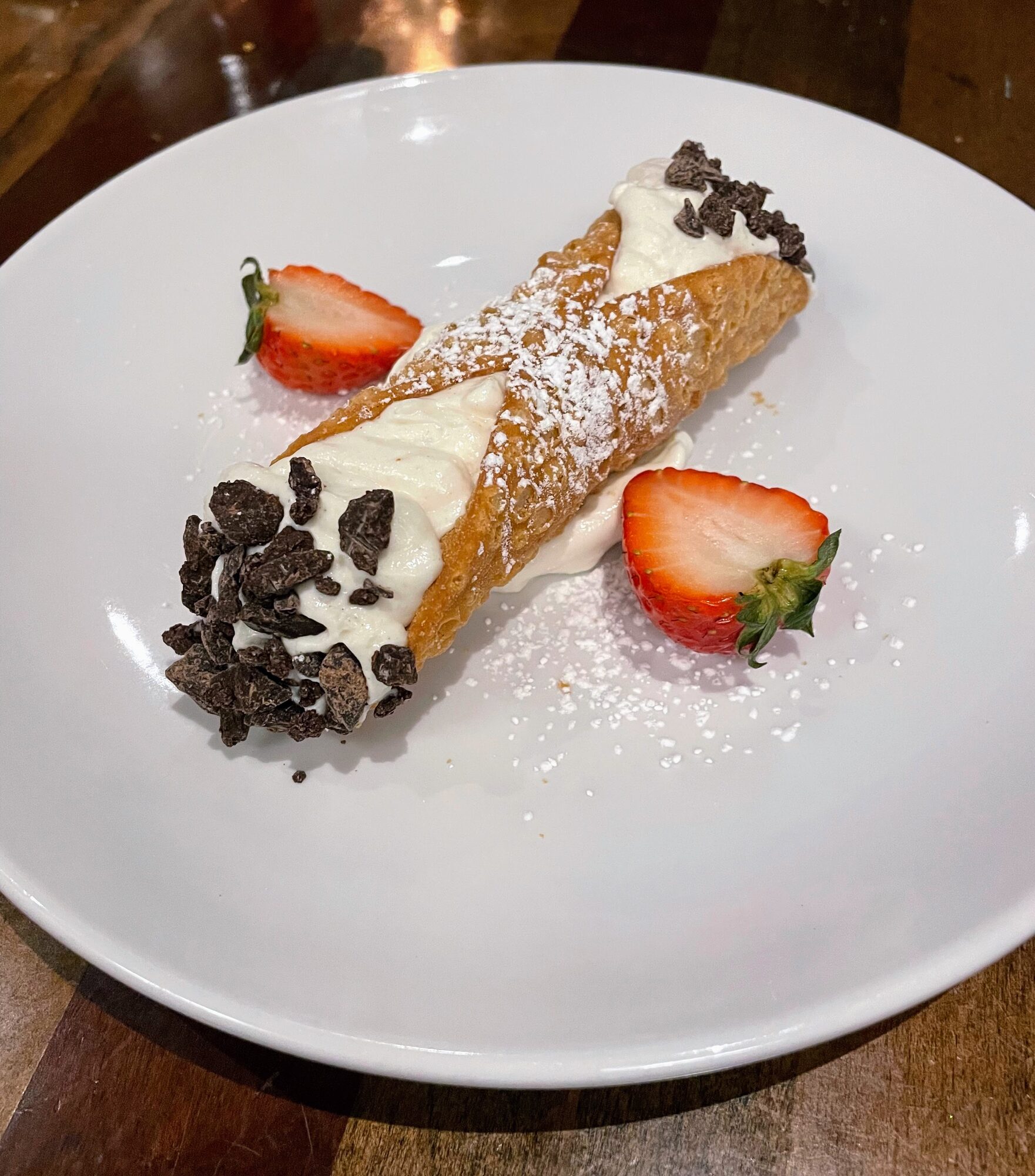 A cannoli dusted with powdered sugar and rolled in chocolate chips, plated with fresh strawberries at Quanto Basta.