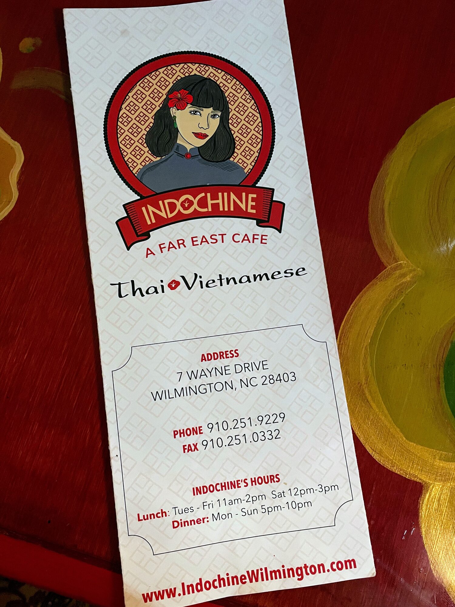 An Indochine restaurant menu resting on a red painted table.
