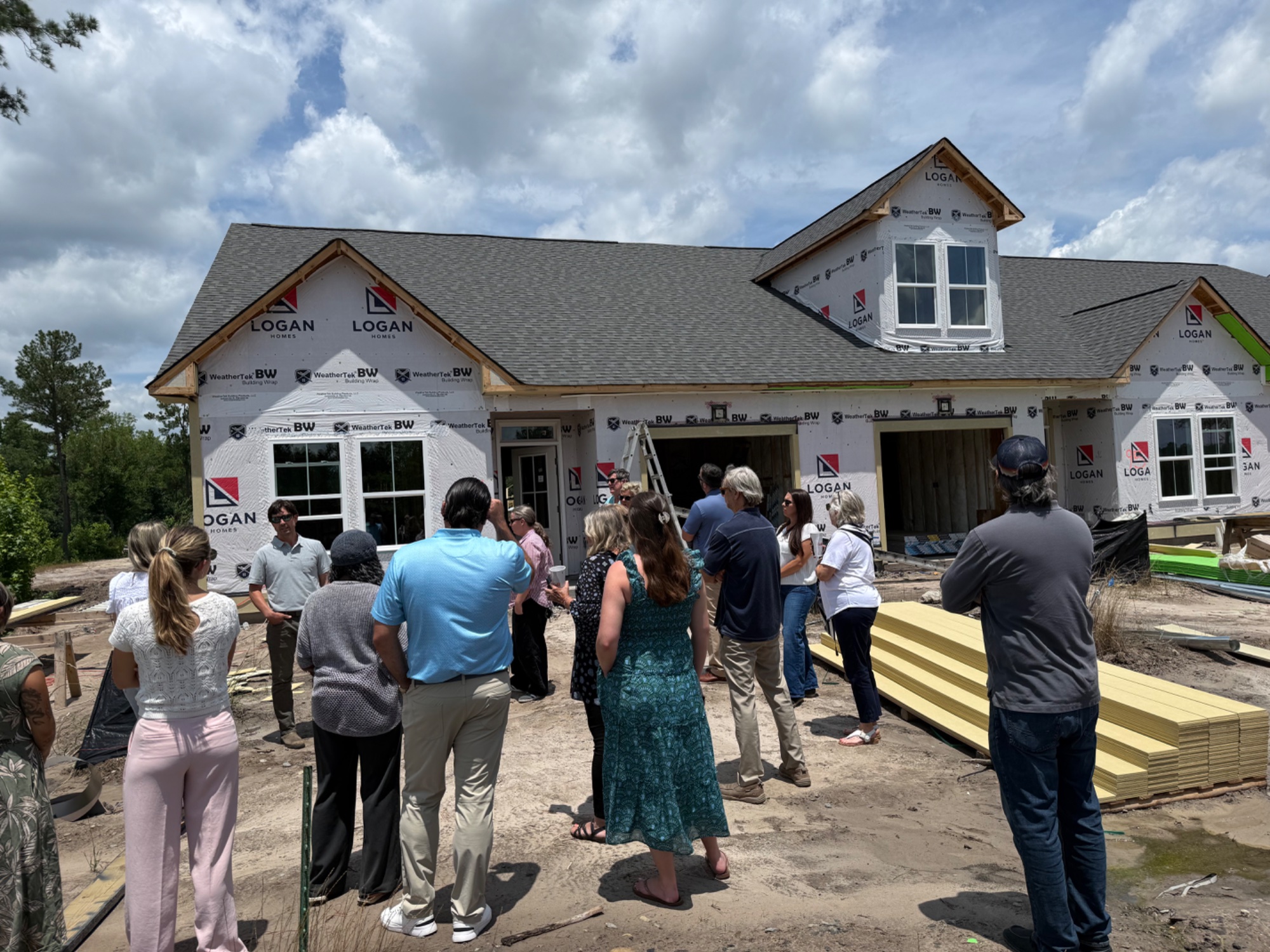 Buyers touring a home under construction wrapped in Logan Homes building paper — a common sight across Leland.