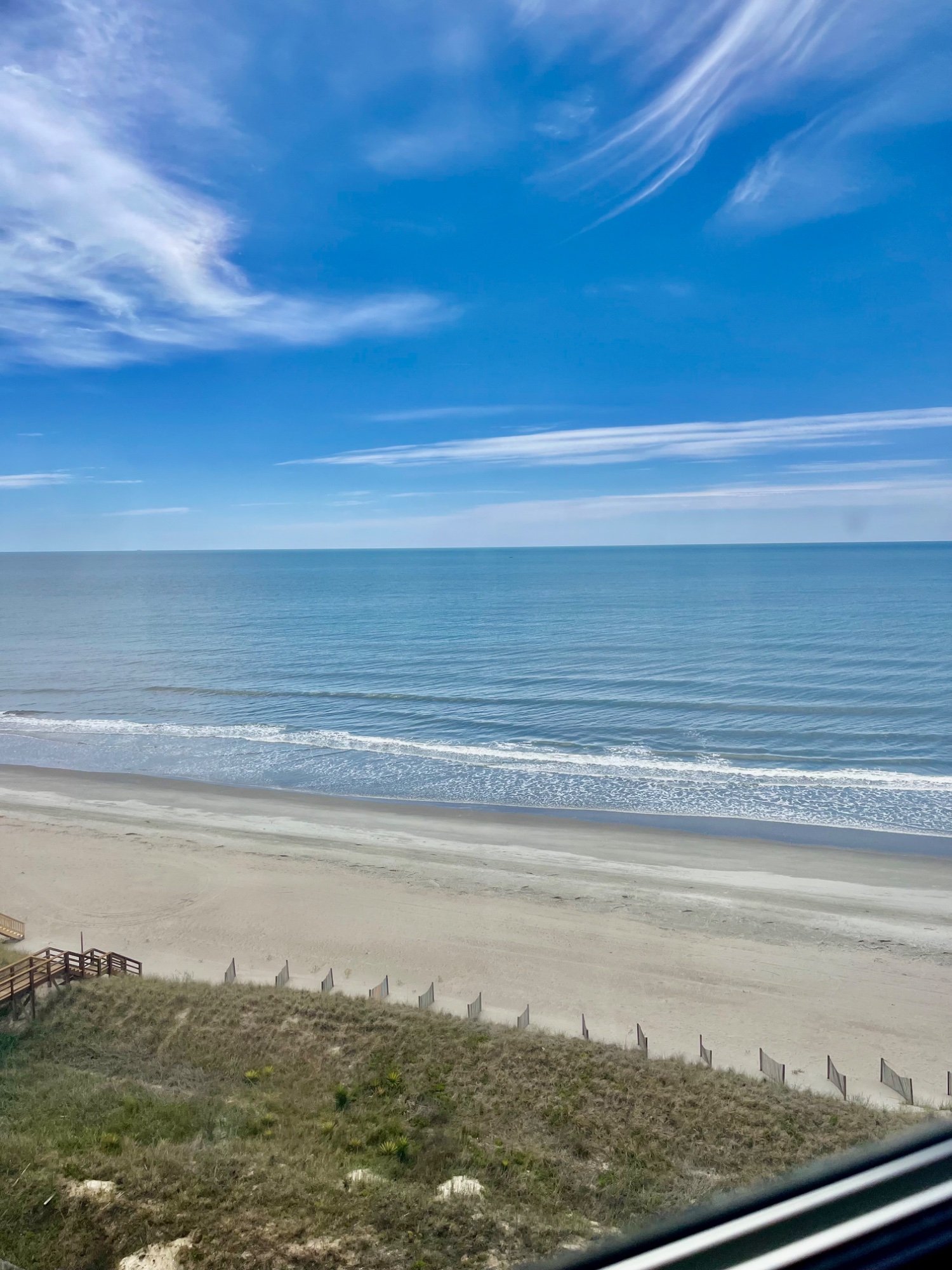 Wide sandy beach and rolling ocean waves seen from an oceanfront balcony under a bright blue sky, North Carolina coast.