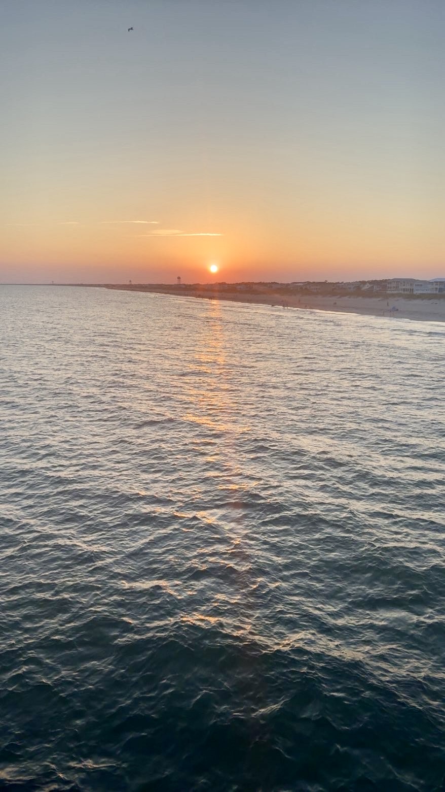 Golden sunset over the Atlantic Ocean with calm water and a distant coastline on the North Carolina coast.